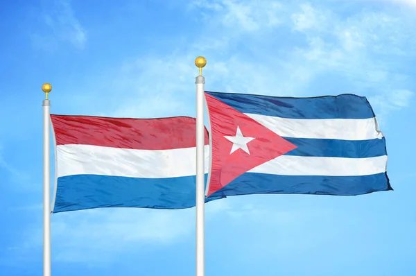 オランダとキューバの旗竿と青い空の背景に2つの旗 — ストック写真