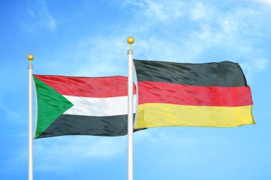 Sudan ve Almanya bayrak direkleri ve mavi bulutlu arka planda iki bayrak