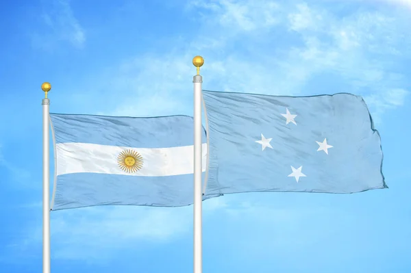 Argentina and Micronesia two flags on flagpoles and blue cloudy sky background