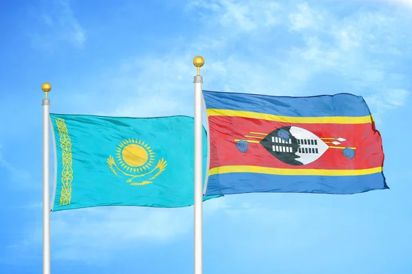 Kazakhstan and Eswatini Swaziland two flags on flagpoles and blue cloudy sky background