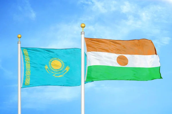 Kazakhstan and Niger two flags on flagpoles and blue cloudy sky background