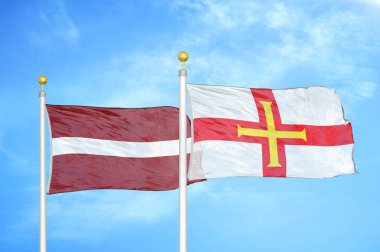 Letonya ve Guernsey bayrak direkleri ve mavi bulutlu arka planda iki bayrak