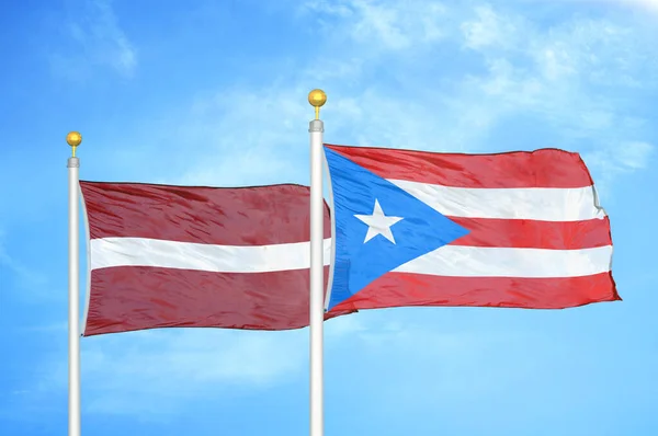 Lotyšsko Portoriko Dvě Vlajky Vlajkových Stožárech Modrá Oblačná Obloha Pozadí — Stock fotografie