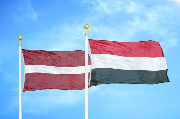ラトビアとイエメンの旗竿と青空の背景に2つの旗 — ストック写真