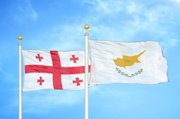 Georgia and Cyprus two flags on flagpoles and blue cloudy sky background