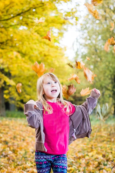 Pretty young girl throws leaves over her head in the park and having great fun.