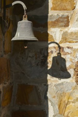 Duvarda gölgeli eski bir gemi çanı asılı.