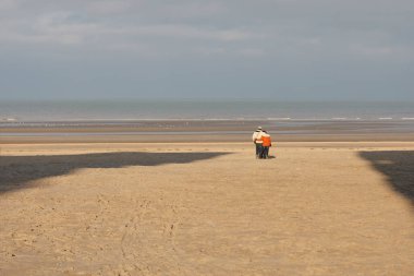 Boş bir sahilde yürüyen yaşlı bir çift.