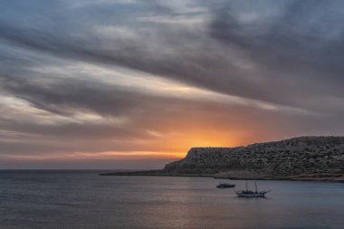Tekneler ve kayalar ile dramatik deniz günbatımı fotoğrafı.