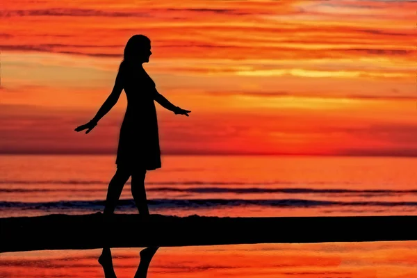 Dancing woman silhouette at the sea with orange sunset sky at background
