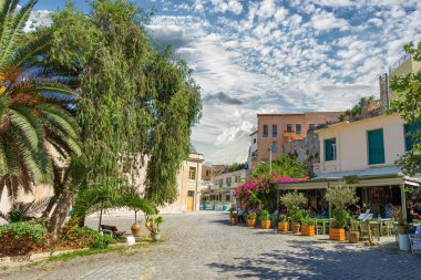 Chania, Yunanistan - Ağustos, 2018: Resmi güzel bulutlar ile Kafe oturan insanlar ile güneşli sokak