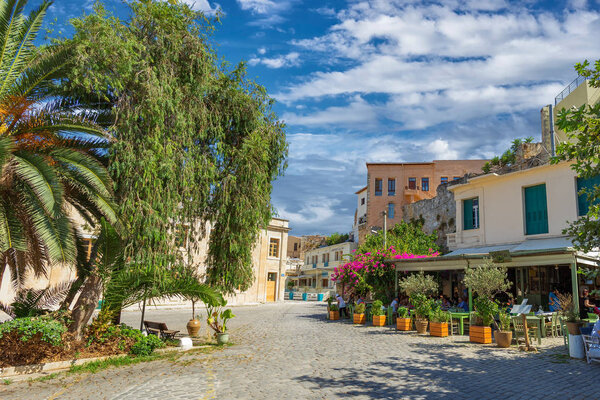 Chania, Greece - August, 2018: Picture of sunny street with people sitting in the cafe, with beautiful blue clouds