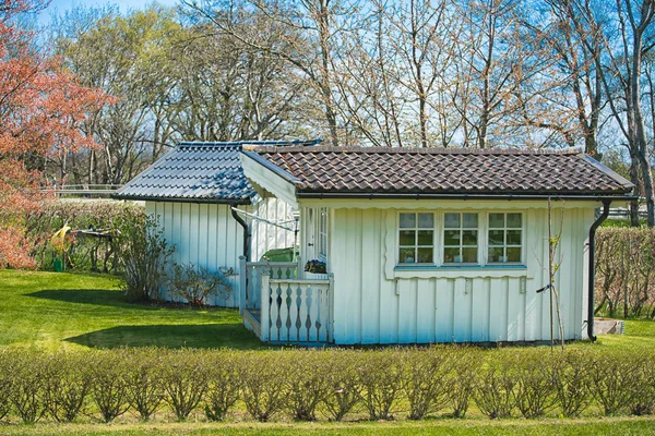 Pequeña casa de verano de madera blanca en el jardín con hierba verde y árboles al fondo — Foto de Stock