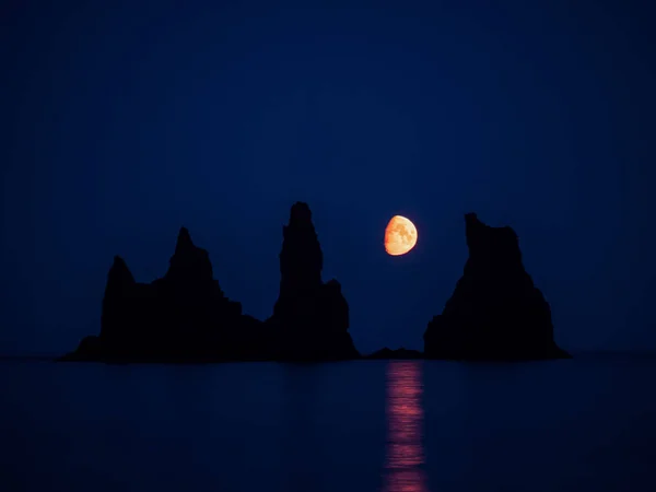 Silueta de formaciones rocosas de basalto Troll Toes en la playa Negro en la noche con la luna entre las rocas. Reynisdrangar, Vik, Islandia — Foto de Stock
