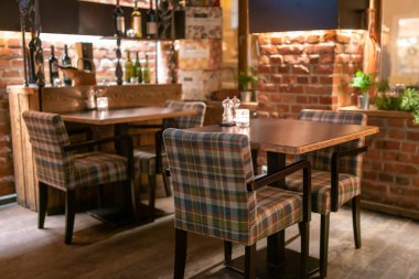 İçi kahverengi ahşap masalar ve gece kareli sandalyelerle dolu çatı katı tarzı bar.