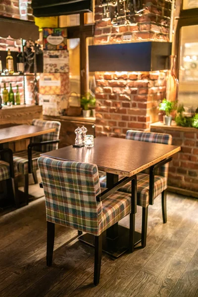 Loft styl bar interiér s hnědými dřevěnými stoly a kostkované židle v noci — Stock fotografie