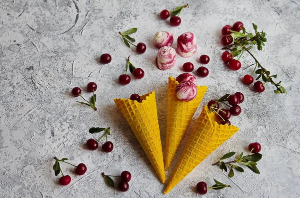 Homemade cherry ice cream with cottage cheese in a colored waffle cone. Healthy dessert, fresh cherry on a light marble background