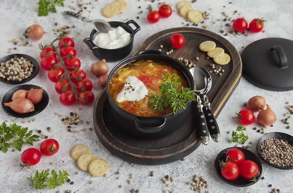 俄罗斯传统的白菜汤 自制的什奇汤 用白菜和西红柿包在一个黑锅里 一些配料 酸奶油 辣椒和淡淡的樱桃 — 图库照片
