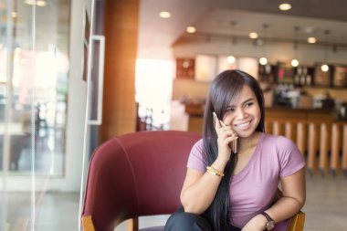 Genç Asyalı güzel bir kadın kafeteryada akıllı telefon kullanıyor..