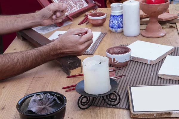 Primo piano delle mani di un artigiano con pennelli e tinta per decorare piastrelle con tecniche tradizionali e artigianali — Foto Stock