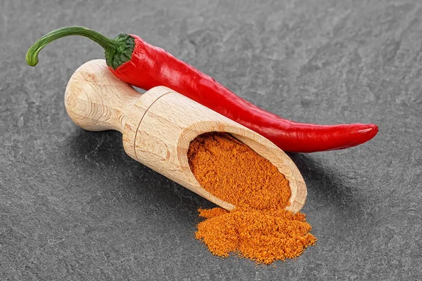 Kırmızı biber biber ve siyah taş masada tahta kaşık toz