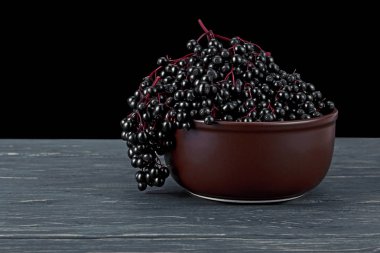 Rustik ahşap masada kil kase siyah mürver meyveleri. Sambucus