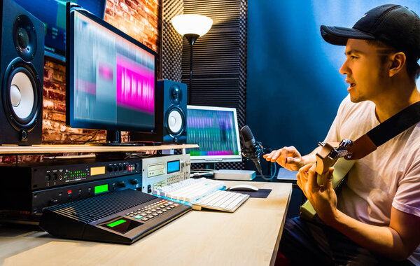 asian male guitarist recording electric guitar track in home studio