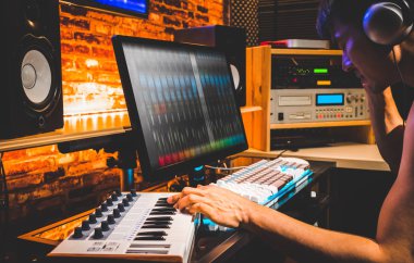 Genç Asyalı erkek besteci bir şarkı ev Studio bilgisayarda düzenlemek için MIDI klavye çalmaya