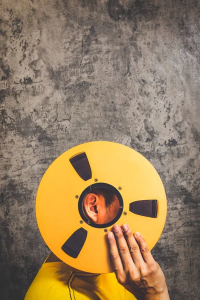 Grunge doku çimento duvar arka plan üzerinde Vintage reel bant tutan adam. müzik, kayıt, film, şarkı konsepti