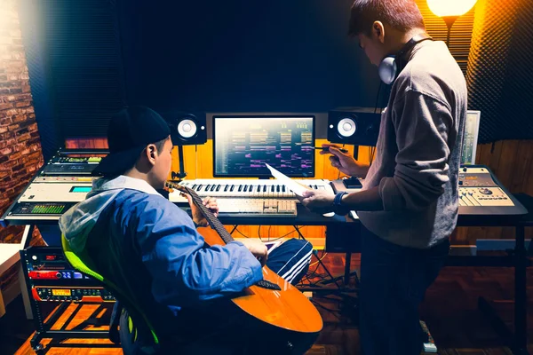 男性アジアのプロデューサーは レコーディングスタジオで録音する曲のスタイルについてプロのギタリストと相談 — ストック写真