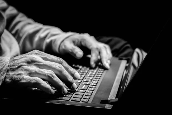 close up BW old man hands surfing internet on laptop computer. old people and technology concept