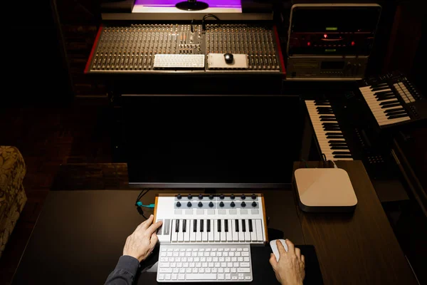 top view of male music producer hands working on midi keyboard and computer in recording studio