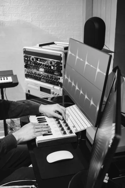 美国黑人和白人男性音乐制作人手工调整Midi键盘旋钮 用于在家庭工作室的计算机监视器上编辑波形 — 图库照片