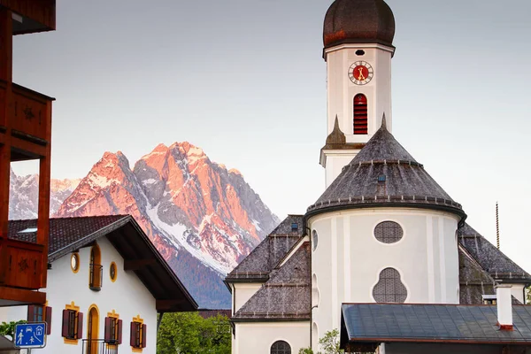 Iglesia en Garmisch con el pico Zugspitze a la luz del sol roja de la mañana —  Fotos de Stock