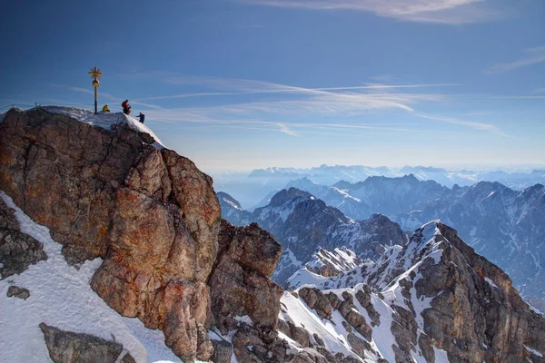 Goldenes Gipfelkreuz und winzige Bergsteiger auf der Zugspitze Stockbild