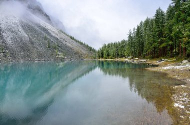 Altay Shavlinskoye shore gölde dağ yamaçlarında kar ile kaplı. Rusya