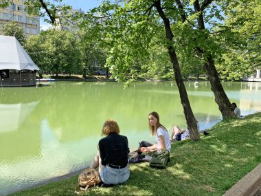 Moskova, Rusya, 20 Haziran 2019. Güneşli Haziran gününde Temiz göletlerin kıyısında dinlenen iki genç kadın