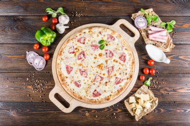 Jambon ve mantar yuvarlak kesme tahtası koyu ahşap arka plan üzerinde büyük pizza. Pizza malzemeleri. Üstten görünüm