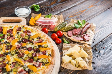Sosis, salatalık turşusu, pastırma yuvarlak kesme tahtası koyu ahşap arka plan üzerinde büyük pizza. Pizza malzemeleri
