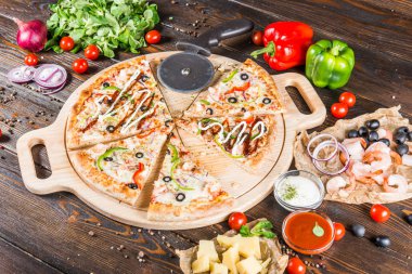 Büyük pizza deniz ürünleri, karides ve zeytin parçalar halinde bir yuvarlak kesme tahtası koyu ahşap arka plan üzerinde kesti. Kesme bıçağı. Gıda katkı maddeleri.