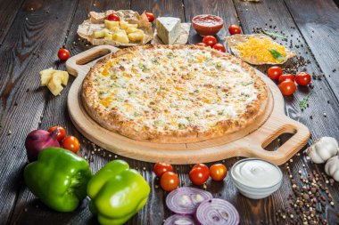 Üç çeşit peynir yuvarlak kesme tahtası koyu ahşap arka plan üzerinde büyük pizza. Malzemeler.