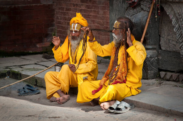 KATHMANDU, NEPAL - AUGUST 14, 2018: Unidentified Hinduist Sadhu with traditional yellow painted faces sitting at Durbar Square, Kathmandu -  Nepal 