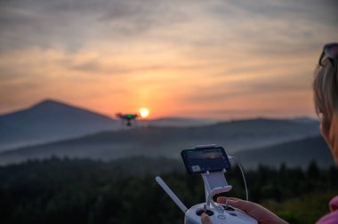 Siluet Drone dağda uçuyor, bulutlarla gün doğumunda gökyüzünde, hava fotoğrafçılığıyla. Dağlar, güneş ve çam ağaçlarıyla kaplı. Gün doğumu