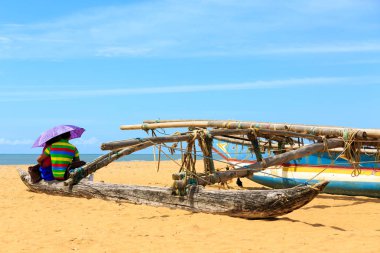 Plajda denize bakan bir şemsiye altında oturan genç çift