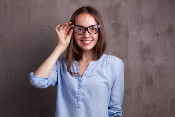 Portret van mooie gelukkig jonge vrouw met bril in de buurt van grijze achtergrond muur — Stockfoto