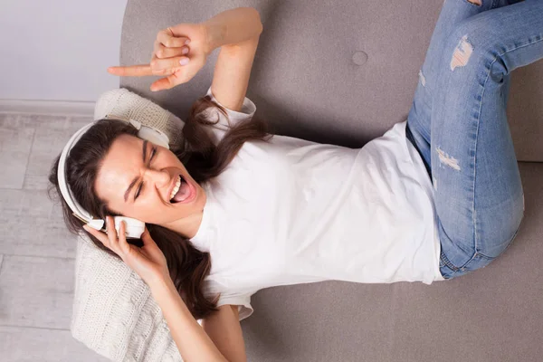 Piękna młoda kobieta szczęśliwa leżąc na kanapie i słuchanie muzyki — Zdjęcie stockowe