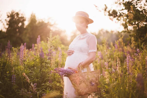 Mujer embarazada sosteniendo una cesta de paja con flores silvestres —  Fotos de Stock