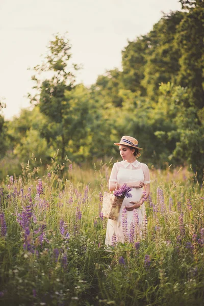 Pregnant woman in white dress holding a straw basket with wildflowers — Stock Photo, Image