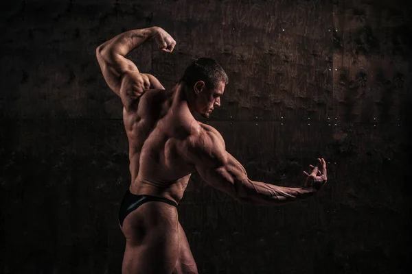 Sportlicher und gesunder muskulöser Mann von hinten auf dunklem Grunge-Hintergrund lizenzfreie Stockbilder
