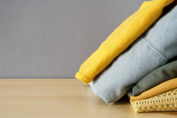 Stack of clothes on wooden table and grey wall background with free space — Stock Photo, Image